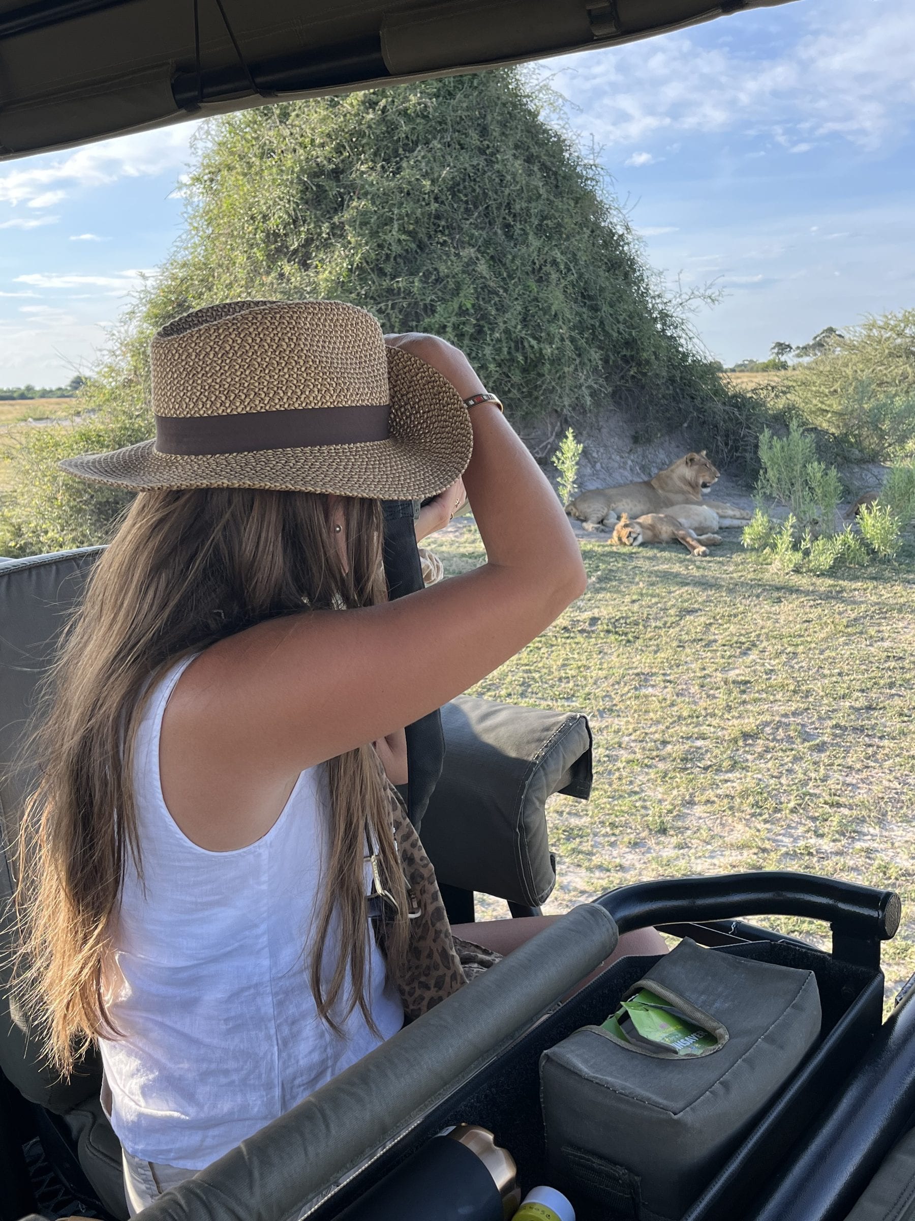 Danielle in a safari vehicle, hat on, looking out through binoculars