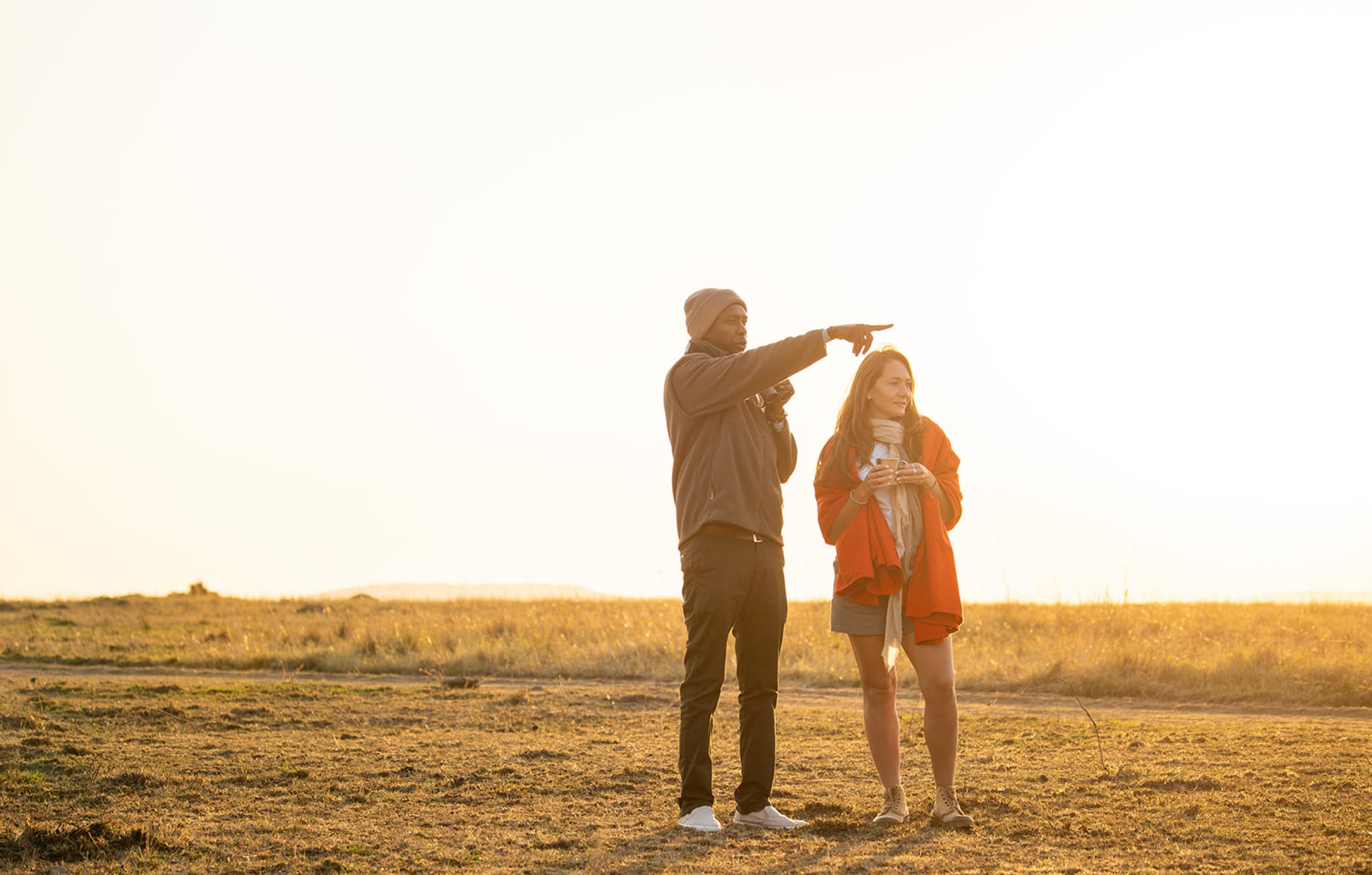 Danielle and a guide silhouetted at sunset, the guide pointing across the plain