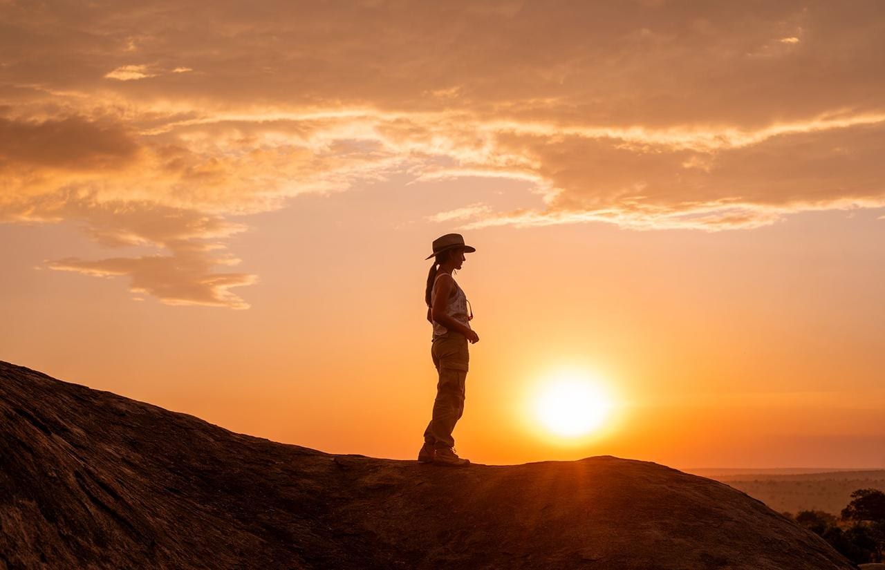Danielle standing on a granite kopje at sunset, silhouetted against the sun