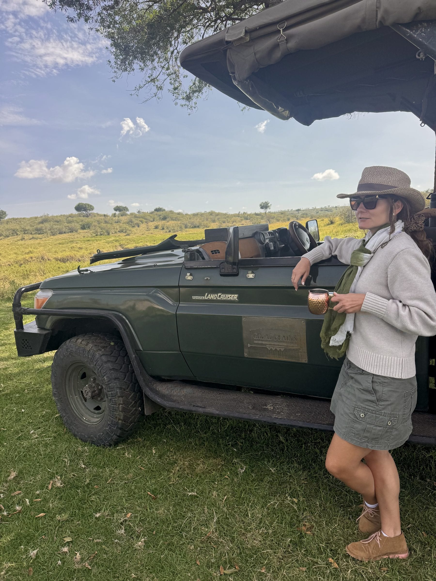 Danielle standing beside an open safari vehicle on the grassland, mug in hand