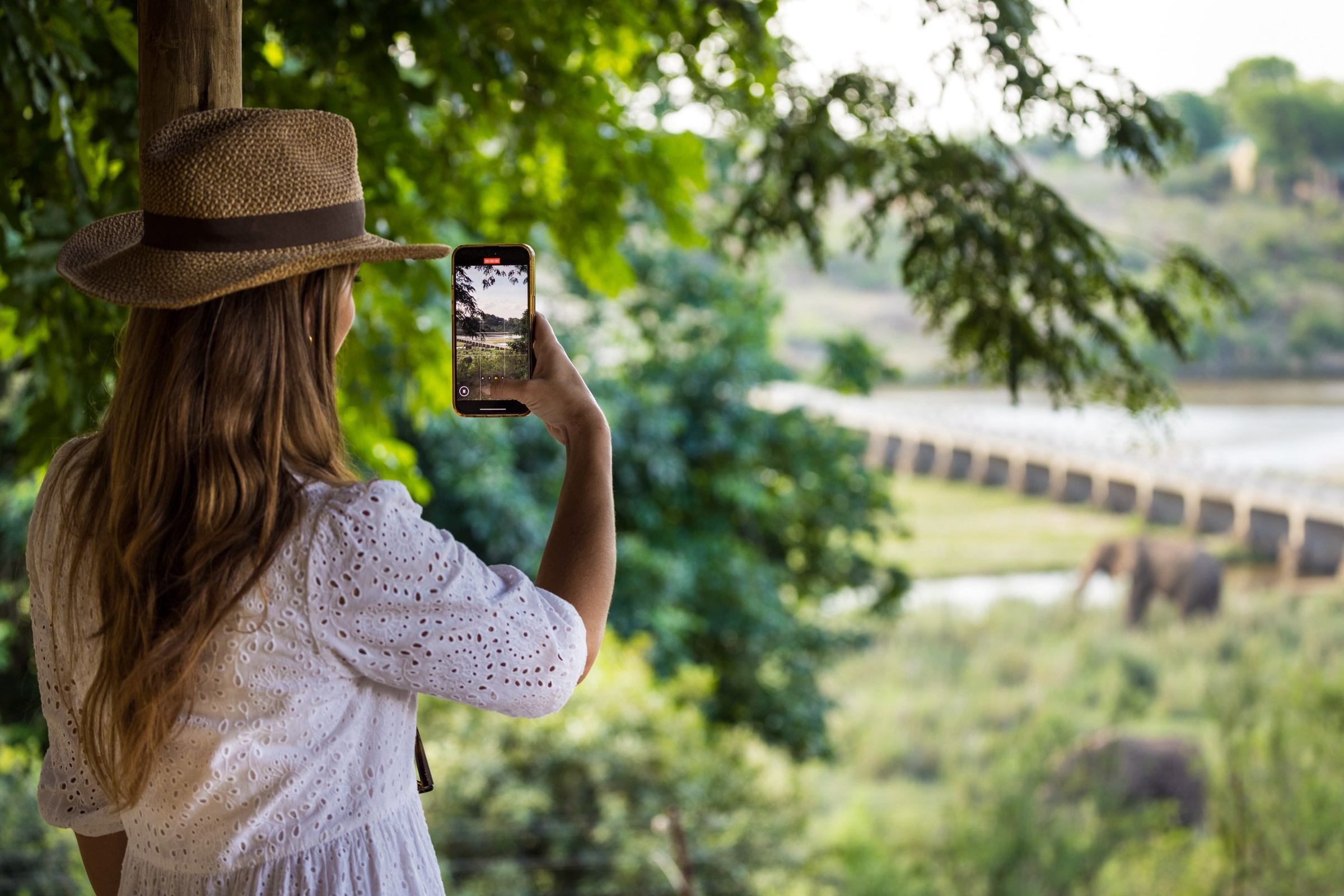 Danielle in a straw hat filming the river and bridge from the deck on her phone
