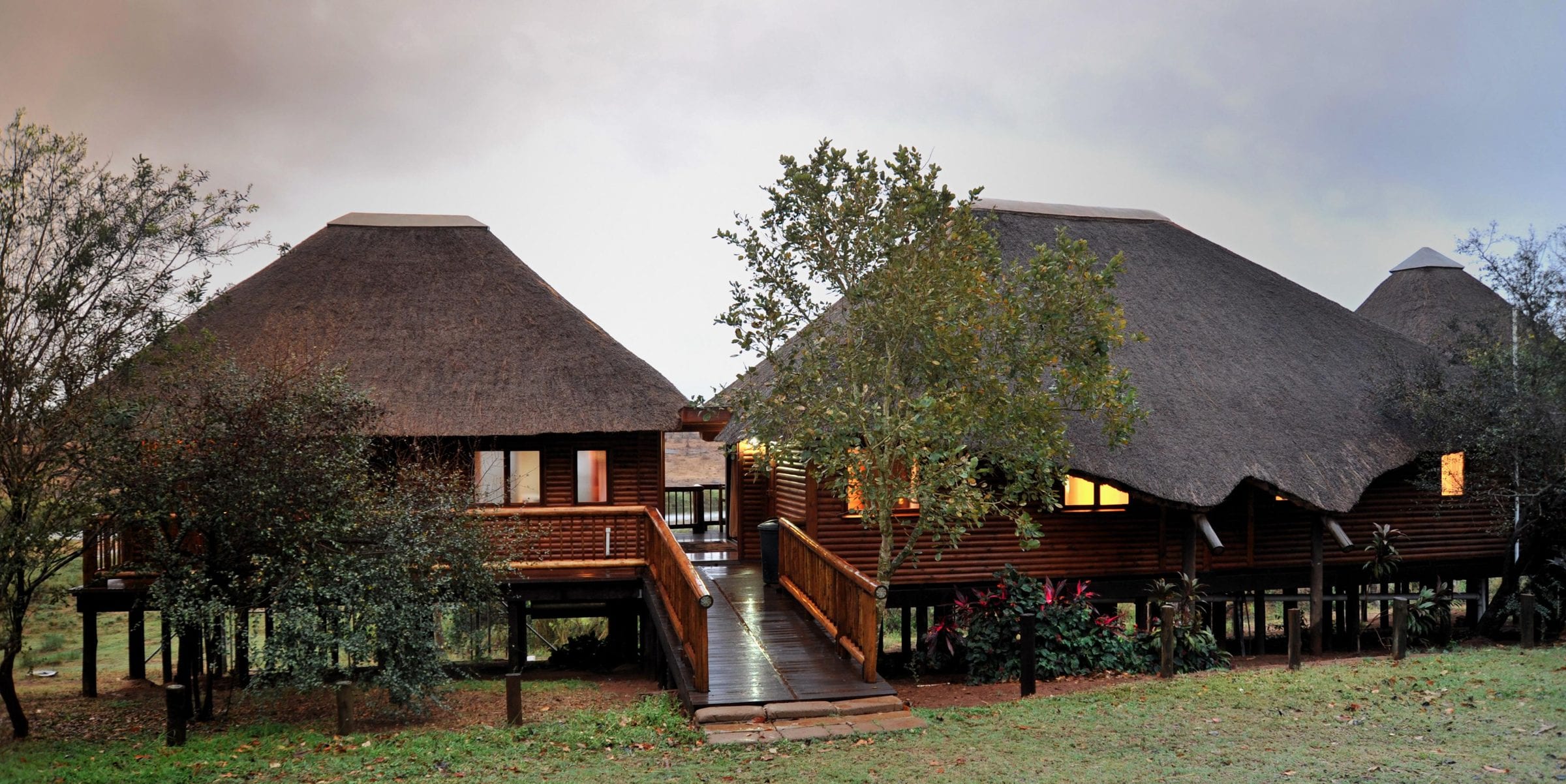 The thatched lodge on stilts at dusk, lamps lit inside