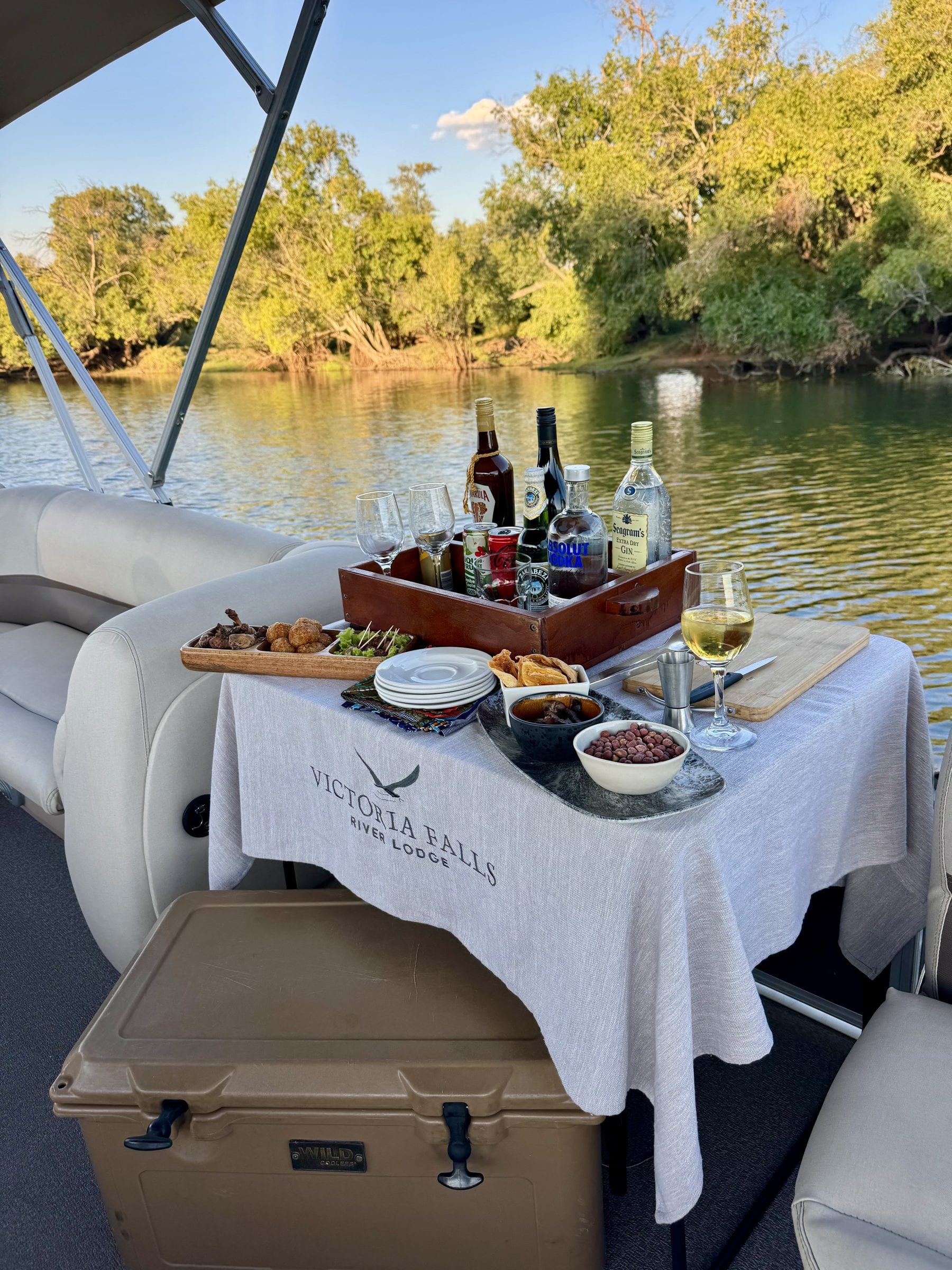 A table laid with wine and lunch on the deck of a river boat, the bank green behind